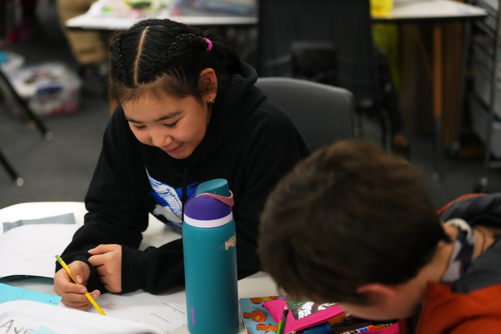 Rayann Martin, a 10-year-old displaced from the village of Kipnuk by ex-Typhoon Halong, left, talks with new classmate Lilly Loewen, 10, right, as they work in the Yup'ik language at College Gate Elementary, Thursday, Oct. 30, 2025, in Anchorage, Alaska. (AP Photo/Lindsey Wasson)