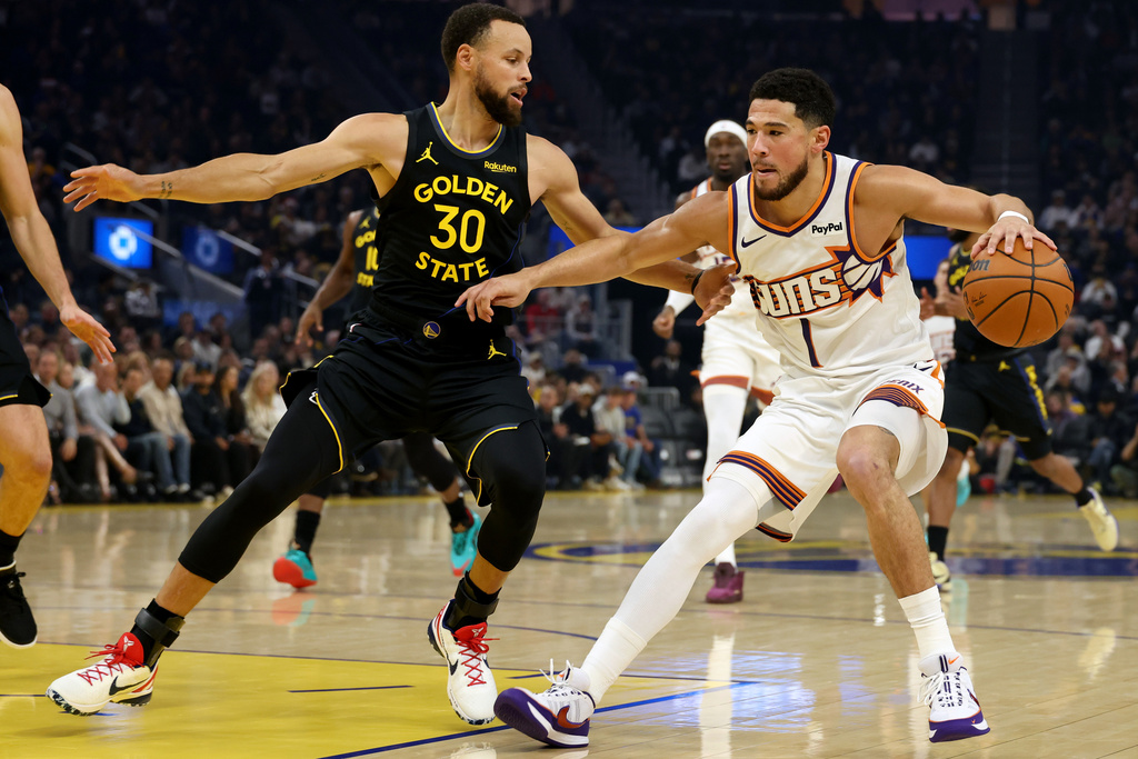 Phoenix Suns guard Devin Booker (1) drives to the basket against Golden State Warriors guard Stephen Curry (30) during the first half of an NBA basketball game in San Francisco, Saturday, Dec. 20, 2025. (AP Photo/Jed Jacobsohn)