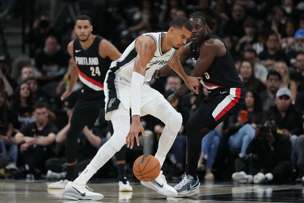 San Antonio Spurs forward Victor Wembanyama (1) drives against Portland Trail Blazers guard Jrue Holiday (5) during the first half in Game 2 of a first-round NBA playoffs basketball series in San Antonio, Tuesday, April 21, 2026. (AP Photo/Eric Gay)