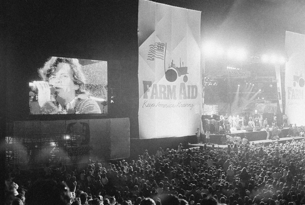 FILE - John Cougar Mellencamp performs both on stage and on one of two large screen television screens set up at the University of Illinois Memorial Stadium in Champaign, Ill. on Sept. 22, 1985 during the Farm Aid concert. (AP Photo/Seth Perlman, file)