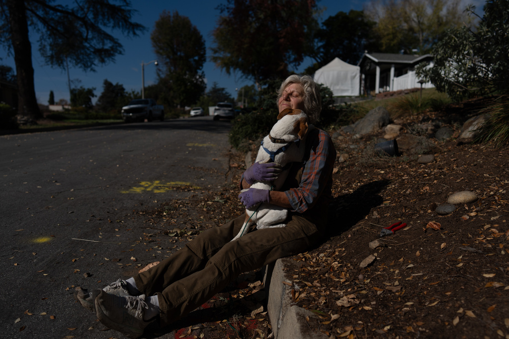 Carolyn Hove, who returned home in July after evacuating during the Eaton Fire, hugs her dog Abby while taking a break from gardening, Wednesday, Dec. 3, 2025, in Altadena, Calif. (AP Photo/Jae C. Hong)