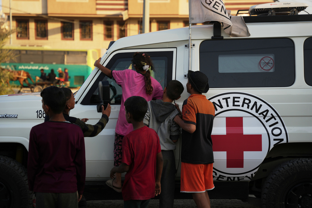 Palestinian kids look into a Red Cross vehicles carrying the bodies of two people believed to be deceased hostages handed over by Hamas make their way toward the Kissufim border crossing with Israel, to be transferred to Israeli authorities, in Deir al-Balah, central Gaza Strip, Thursday, Oct. 30, 2025. (AP Photo/Abdel Kareem Hana)