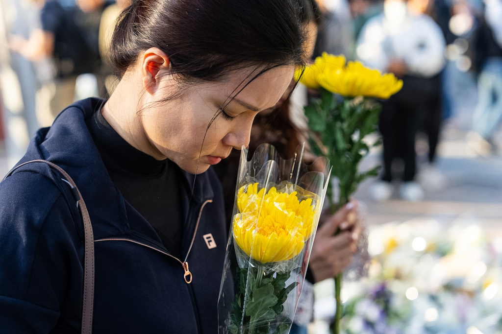 People holds flower near the site to mourn the victims of the deadly Wednesday fire at Wang Fuk Court, a residential estate in the Tai Po district of Hong Kong's New Territories on Saturday, Nov. 29, 2025. (AP Photo/Chan Long Hei)