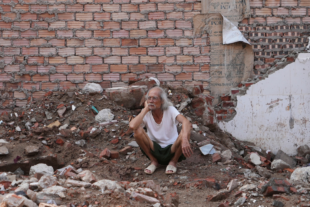A local resident sits on the ground of his demolished house, watching the demolition in his neighborhood to clear site for a new bridge crossing the Red river in Hanoi, Vietnam, Friday, June 5, 2026. (AP Photo/Hau Dinh)