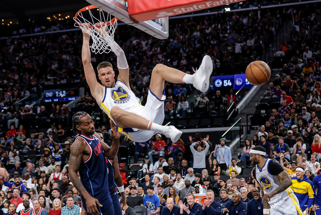 Golden State Warriors' Krystaps Porzingis (7) hangs from the rim after following a missed Stephen Curry (30) shot attemps with a dunk in the first half of an NBA play-in tournament game in Inglewood, Calif., on Wednesday, April 15, 2026. (Carlos Avila Gonzalez/San Francisco Chronicle via AP)