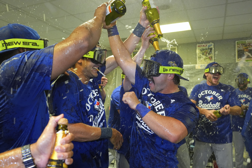Toronto Blue Jays' Davis Schneider, center right, celebrates with teammates in the clubhouse after their baseball game against the Kansas City Royals, Sunday, Sept. 21, 2025, in Kansas City, Mo. (AP Photo/Charlie Riedel)