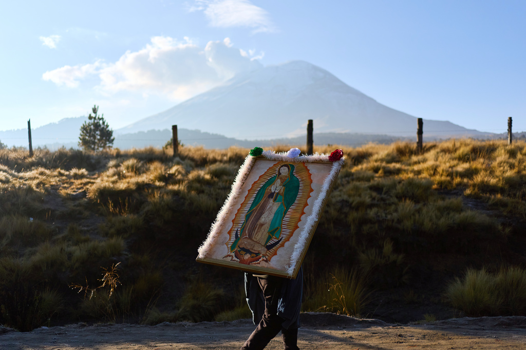 A pilgrim carries an image of the Virgin of Guadalupe past the Popocatepetl in Paso de Cortes on his way to Mexico City, Wednesday, Dec. 10, 2025. (AP Photo/Claudia Rosel)
