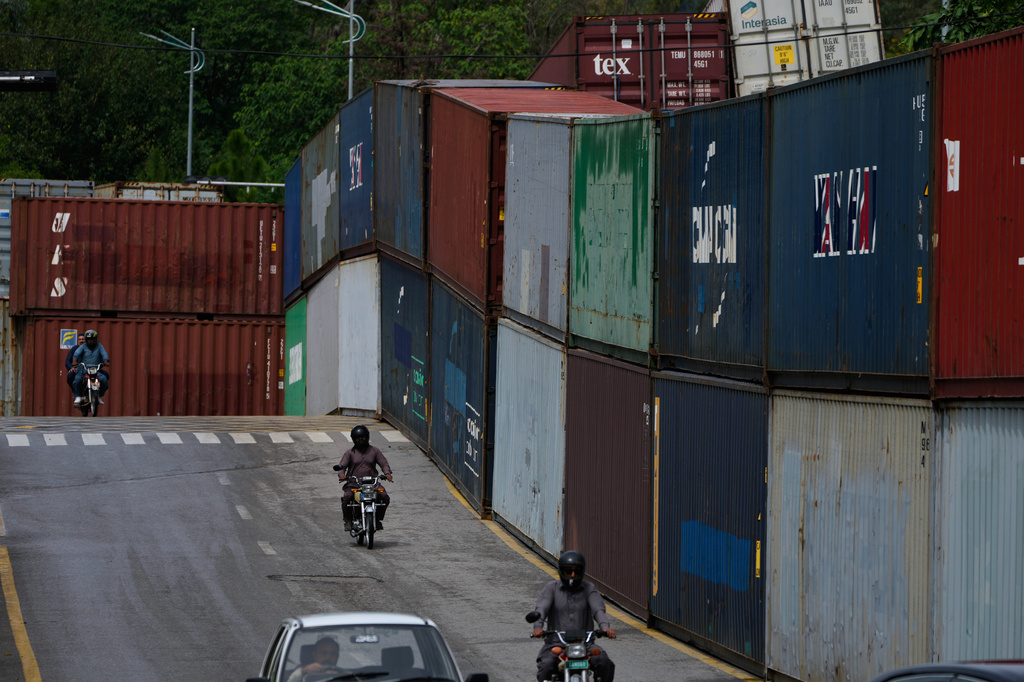 Motorcyclists drive past shipping containers placed by authorities to seal off an area ahead of a plan protest march by the supporters of imprisoned former Prime Minister Imran Khan demanding his release, in Islamabad, Pakistan, Monday, Sept. 28, 2026. (AP Photo/Anjum Naveed)