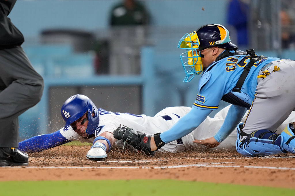 Los Angeles Dodgers' Miguel Rojas, left, scores on a single by Ben Rortvedt as Milwaukee Brewers catcher William Contreras tries to tag him without the ball after missing the throw during the fifth inning of a baseball game Thursday, Aug. 13, 2026, in Los Angeles. (AP Photo/Mark J. Terrill)