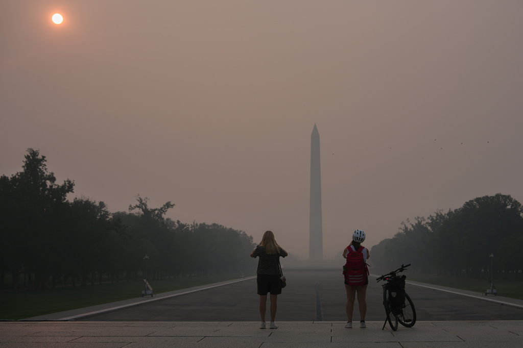 FILE - The sun is obscured by wildfire smoke as people stop to photograph the Washington Monument and Lincoln Memorial Reflecting Pool, July 17, 2026, on the National Mall in Washington. (AP Photo/Julia Demaree Nikhinson, File)