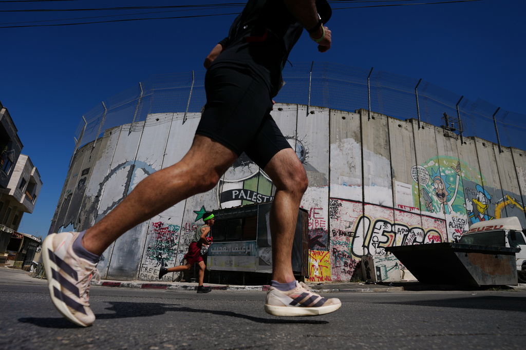 Runners pass by Israel's separation wall as they compete in the Palestine Marathon in the West Bank city of Bethlehem, Friday, May 8, 2026. (AP Photo/Mahmoud Illean)