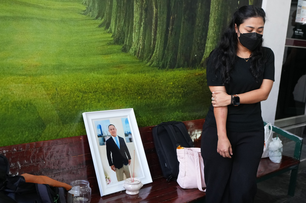 A relative of a musician Preutthipong Pudmon victim, a victim in a music bar fire, stands beside his portrait as she receives his body at a police hospital in Bangkok, Thailand, Wednesday, July 15, 2026. (AP Photo/Sakchai Lalit)