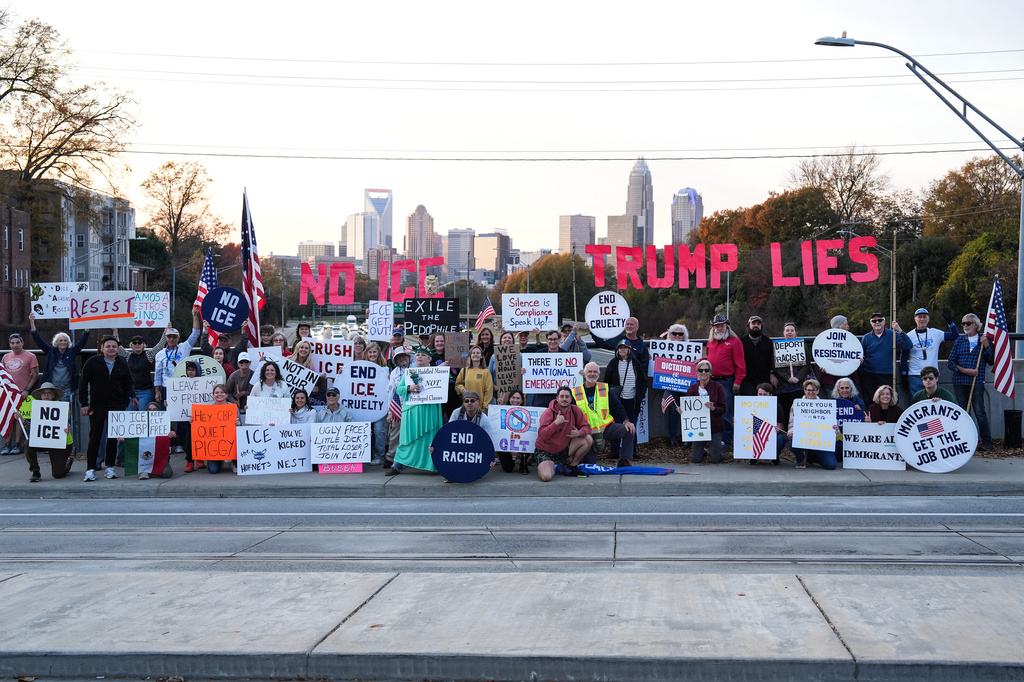 Protesters pose for a photo as they hold signs amid the arrival of federal law enforcement, Tuesday, Nov. 18, 2025, in Charlotte, N.C. (AP Photo/Matt Kelley)