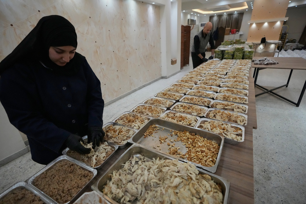 Volunteers prepare meals to be distributed for displaced people who fled Israeli strikes from south Lebanon at al-Rahma centre, in the southern port city of Sidon, Lebanon, Saturday, March 14, 2026. (AP Photo/Mohammed Zaatari)