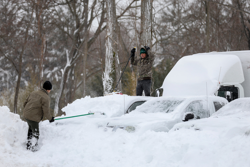 Men clear snow off of cars and trucks in a parking lot, Monday, Feb. 23, 2026, in St. James, N.Y. (AP Photo/Heather Khalifa)