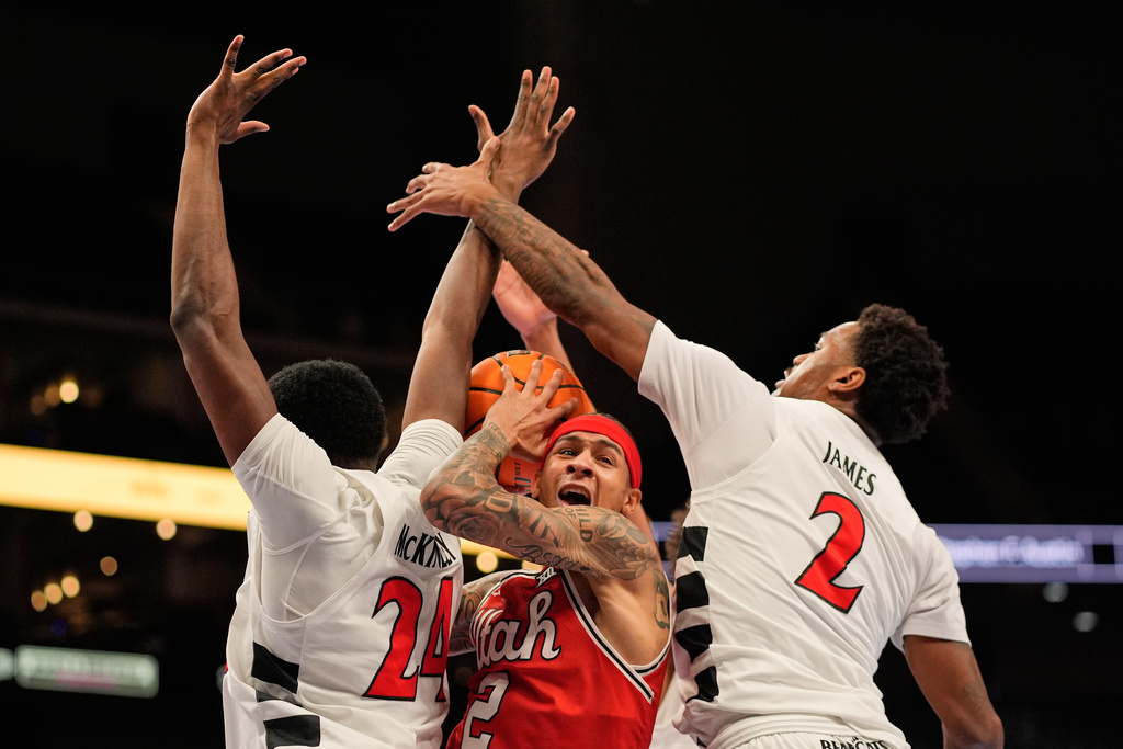 Utah guard Terrence Brown, center, looks to pass under pressure from Cincinnati forward Tyler McKinley (24) and guard Jizzle James (2) during the first half of an NCAA college basketball game at the Big 12 Conference tournament Tuesday, March 10, 2026, in Kansas City, Mo. (AP Photo/Charlie Riedel)