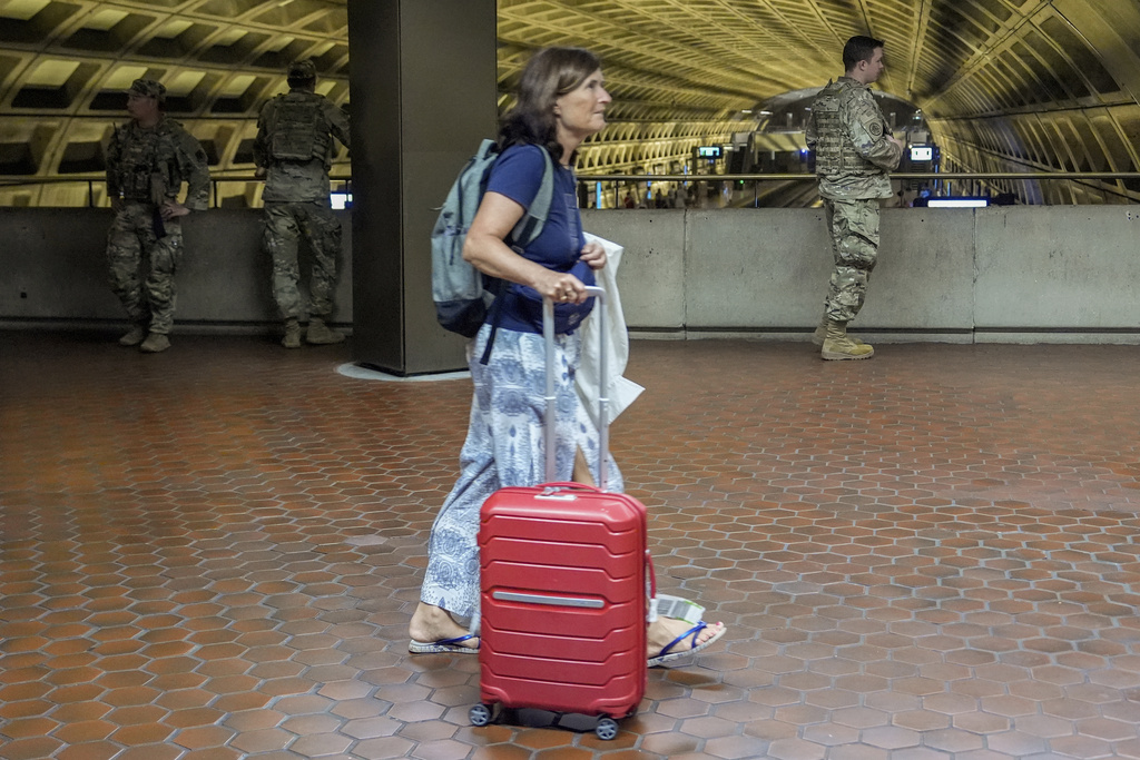 A woman rolls her suitcase past as District of Columbia National Guardsmen patrol inside the Gallery Place-Chinatown Metro Station, Sunday, Aug. 17, 2025, in Washington. (AP Photo/Julia Demaree Nikhinson)