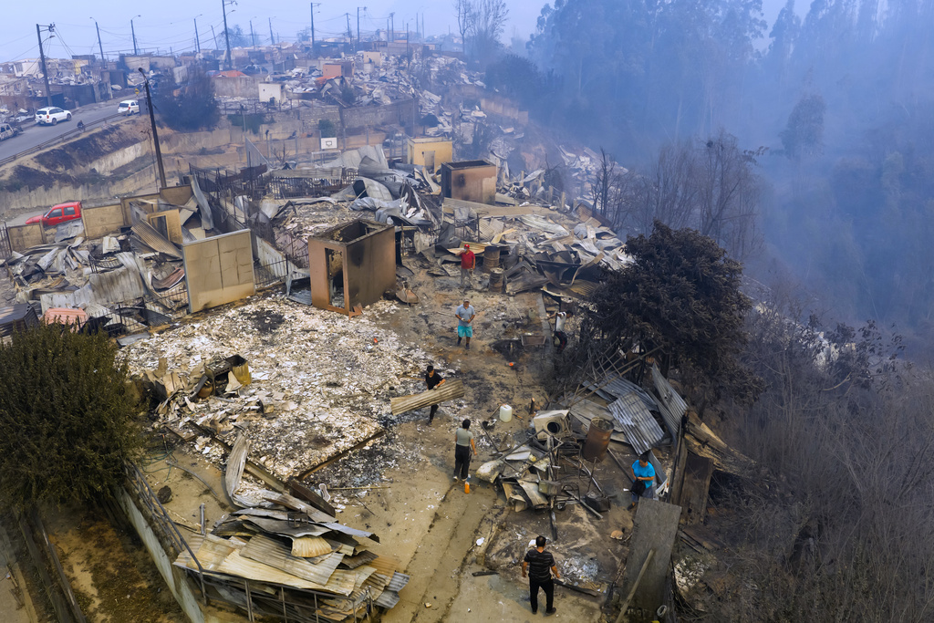 Residents stand by houses burned by wildfires in Lirquen, Chile, Sunday, Jan. 18, 2026. (AP Photo/Javier Torres)