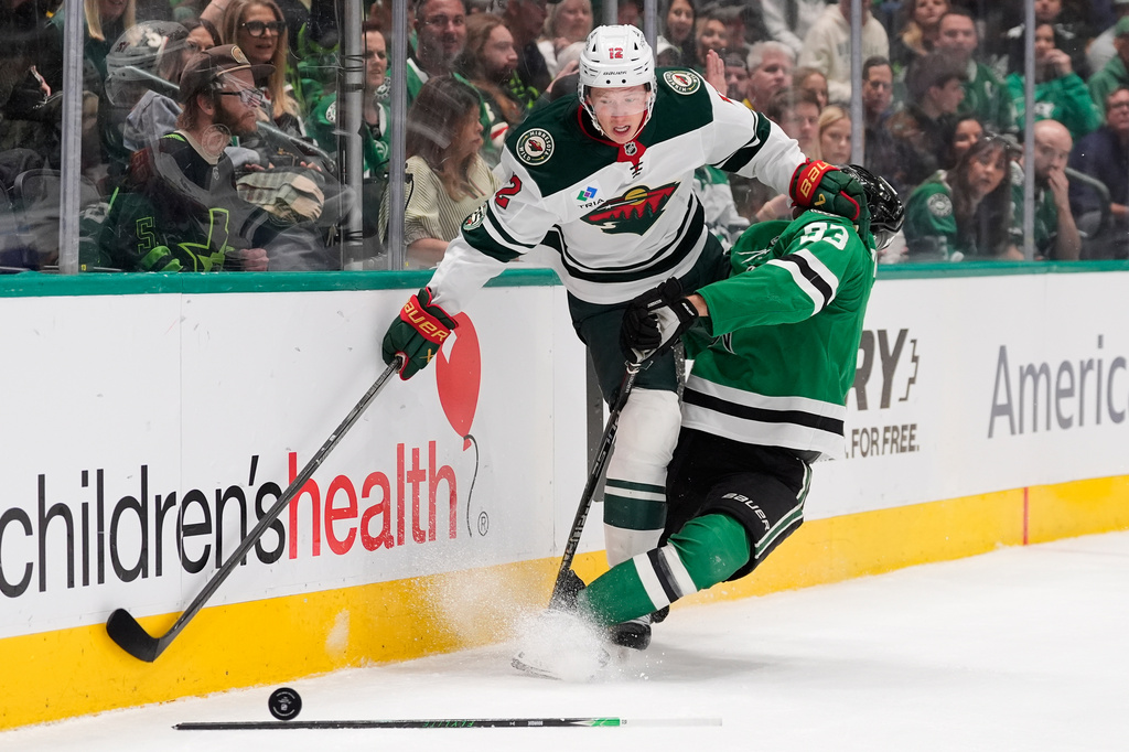Minnesota Wild left wing Matt Boldy (12) and Dallas Stars center Wyatt Johnston (53) slam into the boards chasing after the puck in the first period of an NHL hockey game Thursday, April 9, 2026, in Arlington, Texas. (AP Photo/Tony Gutierrez)