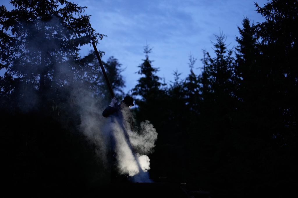 Immo Feldmer uses a pole as he stands on a mound of earth at his family-run, traditional charcoal production site near Hasselfelde in Germany's Harz forest, late Monday, July 6, 2026. (AP Photo/Matthias Schrader)