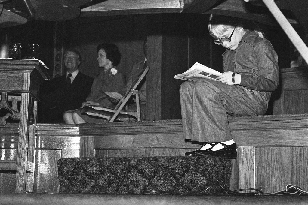 FILE - Amy Carter catches up on her reading as she waits with her parents, Jimmy and Rosalynn Carter, for the Democratic presidential candidate to address a rally at the Tabernacle Baptist Church on Chicago's South Side, Oct. 10, 1976. (AP Photo/Jack Thornell, File)