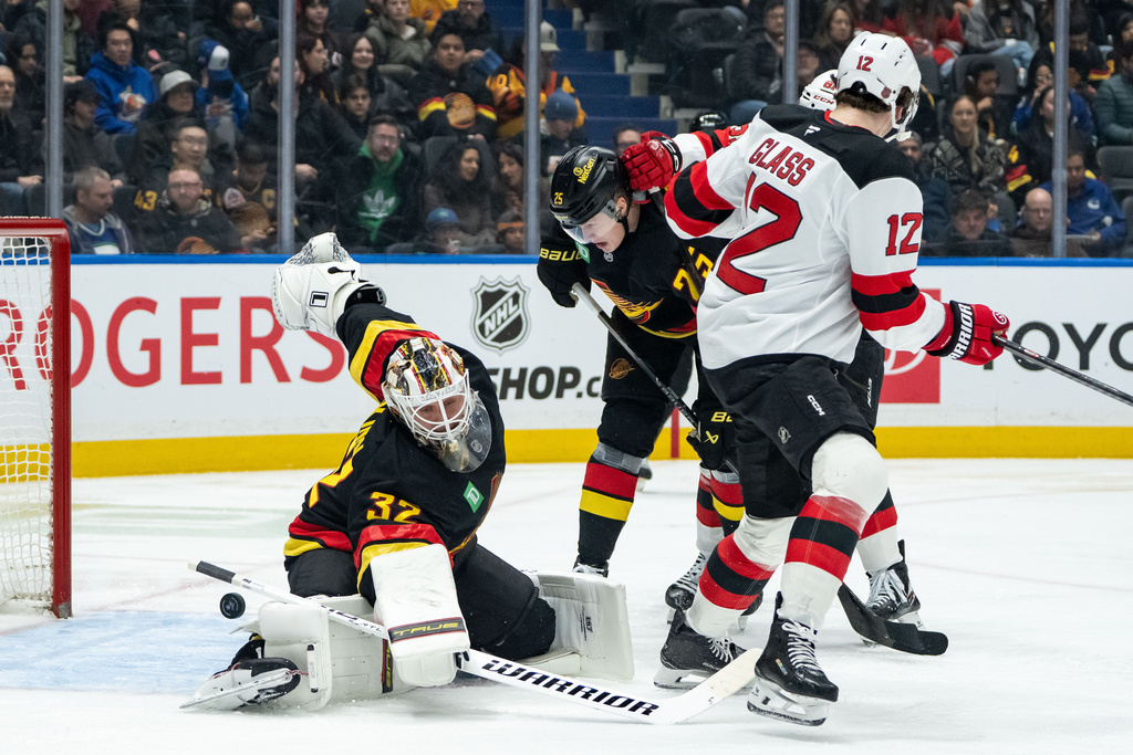 New Jersey Devils' Cody Glass (12) scores against Vancouver Canucks goaltender Kevin Lankinen (32) as Canucks' Elias Pettersson (25) watches during the second period of an NHL hockey game in Vancouver, British Columbia, Friday, Jan. 23, 2026. (Ethan Cairns/The Canadian Press via AP)