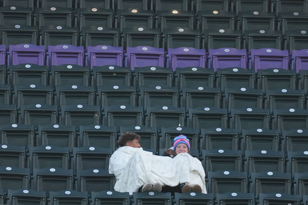 Fans use a blanket to keep warm as temperatures drop to near freezing as the Colorado Rockies host the New York Mets in the second inning of a baseball game, Wednesday, May 6, 2026, in Denver. (AP Photo/David Zalubowski)