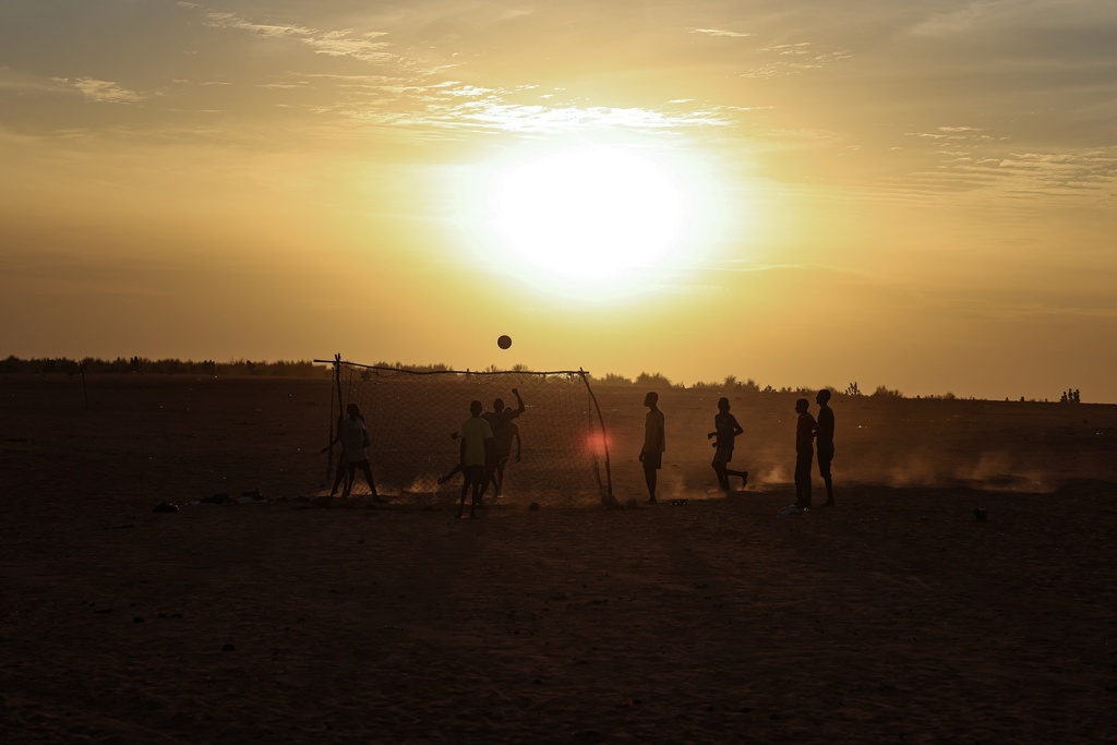 Boys play football as the sun sets in the Mbera Refugee Camp, near Bassikounou, Hodh El Chargui Region, Mauritania, Saturday Nov. 8, 2025. (AP Photo/Caitlin Kelly)