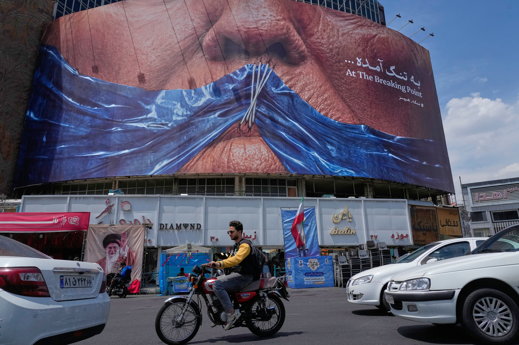 Vehicles drive past a billboard with graphic showing Strait of Hormuz and sewn lips of U.S. President Donald Trump in a square in downtown Tehran, Iran, Saturday, May 2, 2026. (AP Photo/Vahid Salemi)