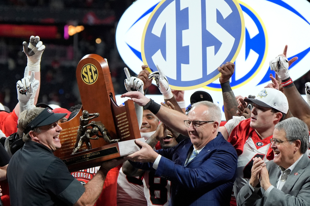 FILE - Georgia head coach Kirby Smart is handed the SEC trophy by Commissioner Greg Sankey as the team celebrates after a Southeastern Conference championship NCAA college football game against Alabama, Dec. 6, 2025, in Atlanta. (AP Photo/Mike Stewart, File)