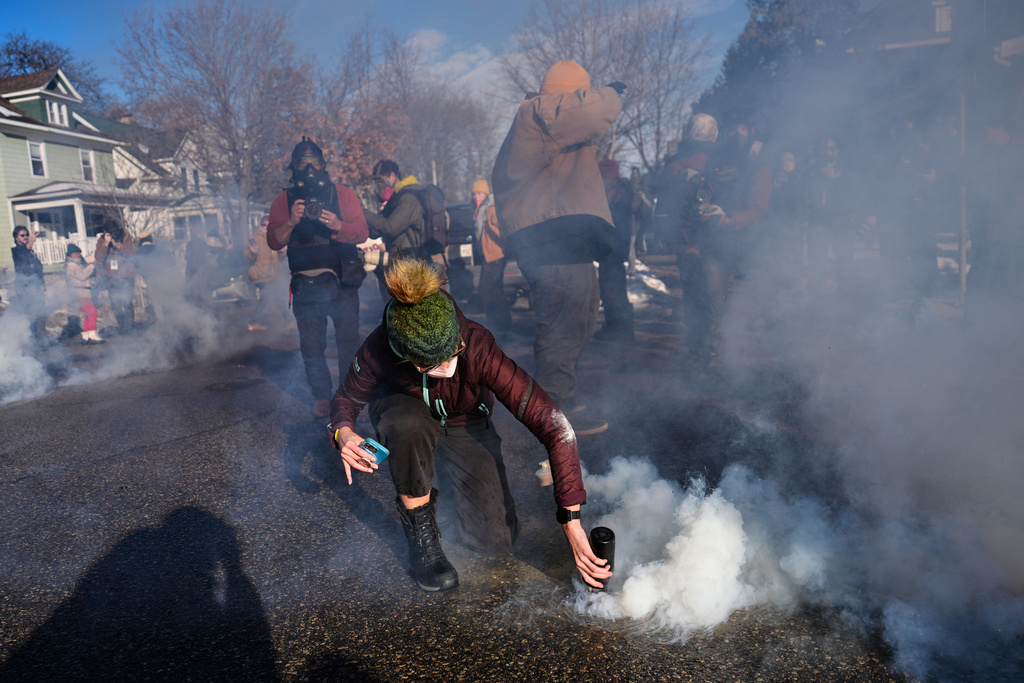 A protester grabs a tear gas grenade deployed by federal immigration officers near the scene where Renee Good was fatally shot by an ICE officer last week, Tuesday, Jan. 13, 2026, in Minneapolis. (AP Photo/John Locher)
