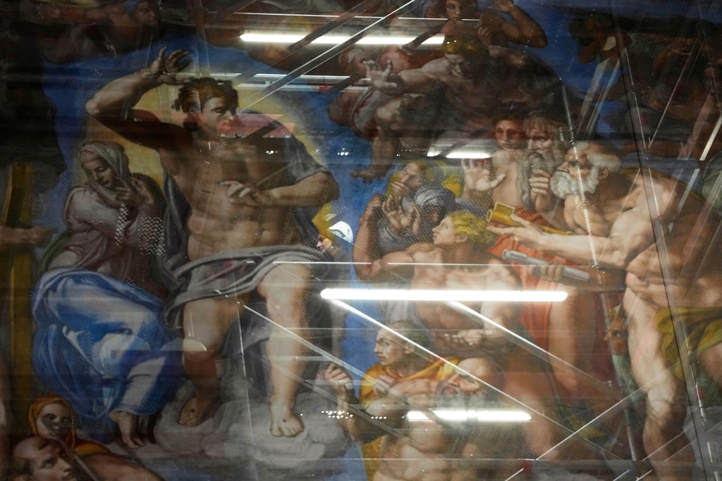 A woman walks behind a screen with a replica of “The Last Judgment,”superimposed on it that covers the scaffolding used for its extraordinary maintenance during a presentation for press in the Sistine Chapel at the Vatican, Saturday, Feb. 28, 2026. (AP Photo/Alessandra Tarantino)