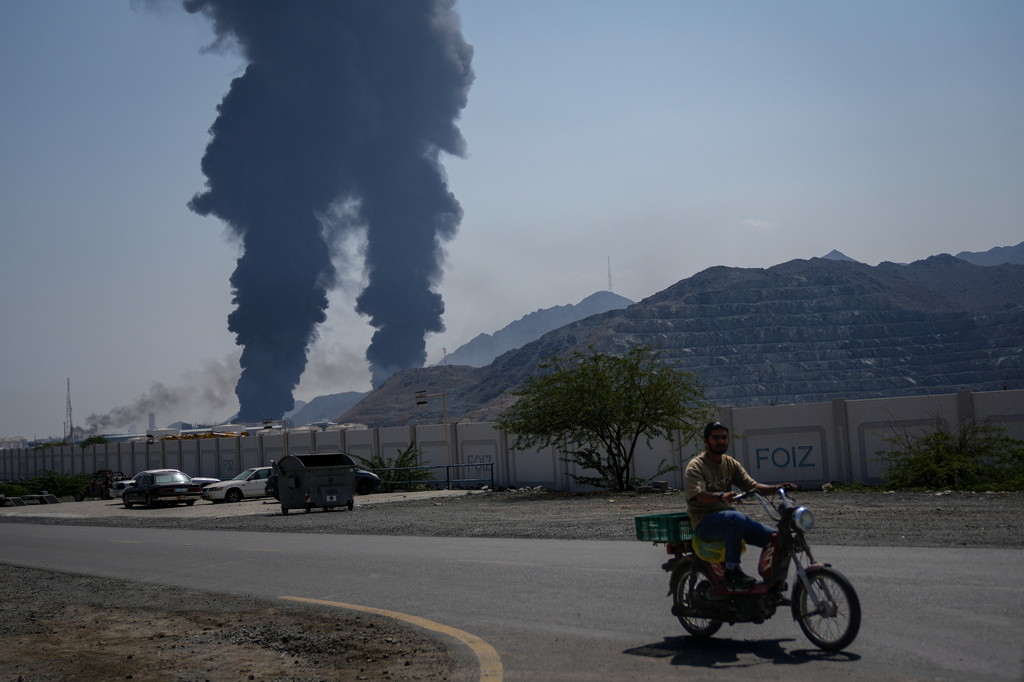 FILE - A man rides a bike as fires and plumes of smoke rise after debris from an intercepted Iranian drone struck an oil facility, according to authorities, in Fujairah, United Arab Emirates, March 14, 2026. (AP Photo/Altaf Qadri, File)