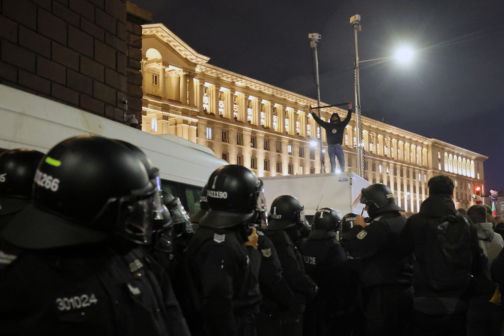 Protester stands on top of a police vehicle as thousands took the streets of Bulgaria's capital, Sofia, to denounce steep tax hikes in next year's draft budget before being finally voted on in parliament, Wednesday, Nov 26, 2025. (AP Photo/Valentina Petrova)