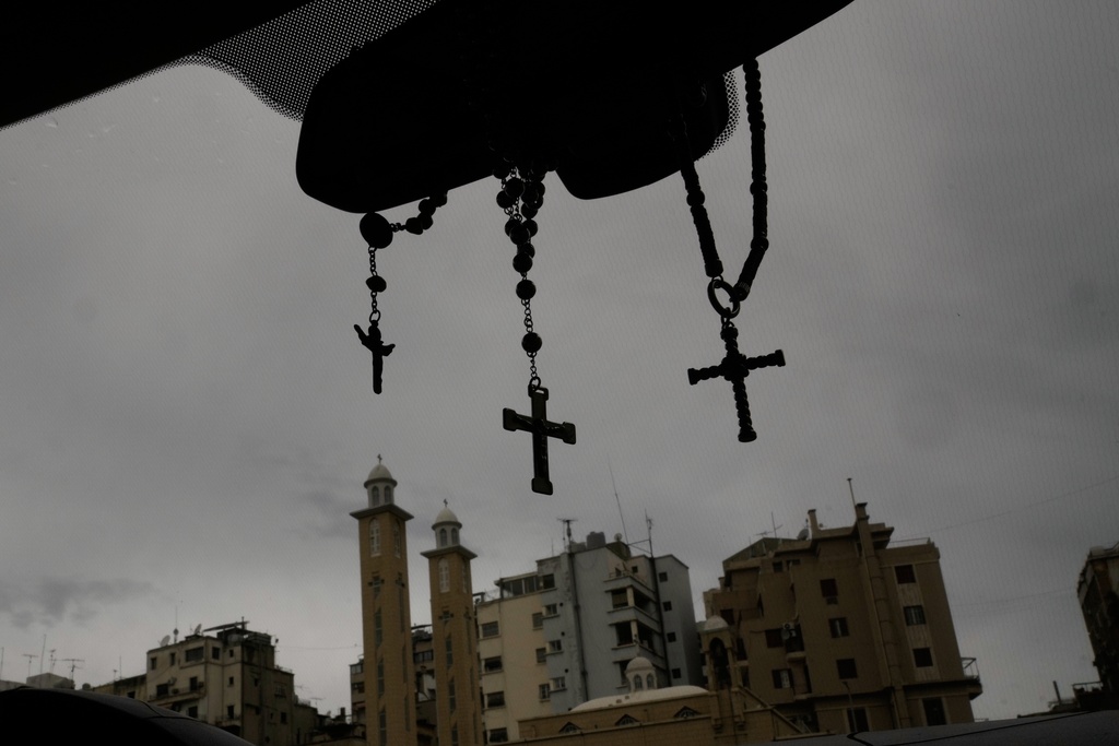 Rosaries and crosses hang from a car's rearview mirror as buildings and church towers rise in the background in Beirut, Lebanon, Friday, Nov. 14, 2025. (AP Photo/Hassan Ammar)