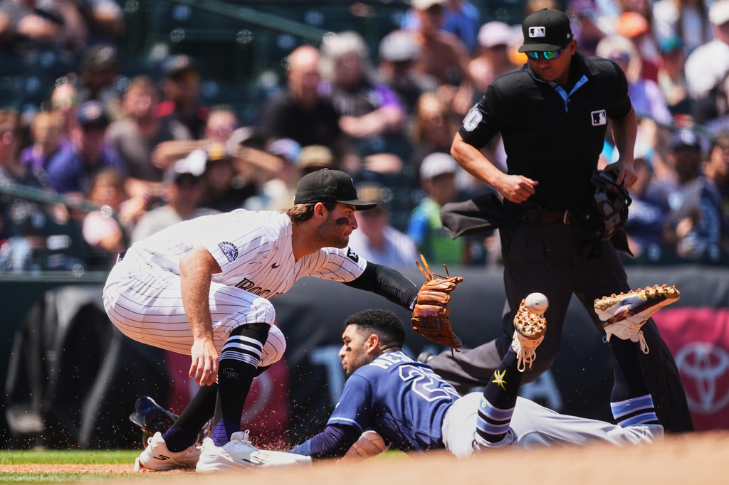 Colorado Rockies third baseman Kyle Karros, front left, fields the throw as Tampa Bay Rays' Victor Mesa Jr. slides safely into third base with a triple while third base umpire Alan Porter waits to make the call in the second inning of a baseball game in Denver, Wednesday, Aug. 5, 2026. (AP Photo/David Zalubowski)
