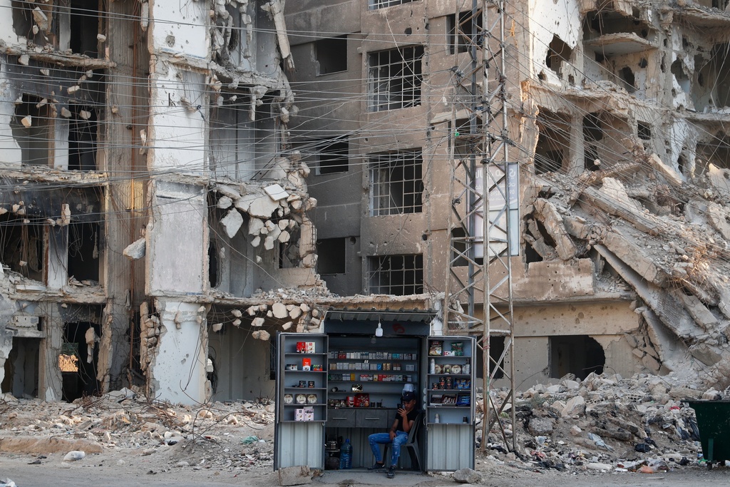 A man waits for customers at a stall beside war-damaged buildings ahead of a parliamentary election set to take place Sunday, in the Damascus suburb of Daraya, Syria, Saturday, Oct. 4, 2025. (AP Photo/Omar Sanadiki)