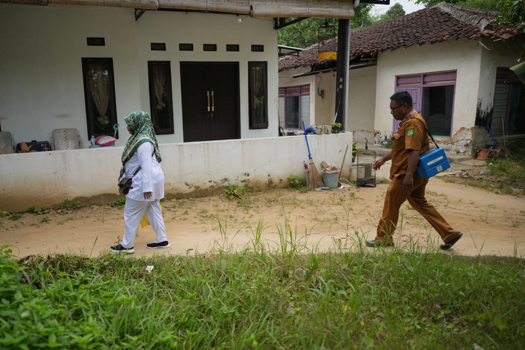 Paramedic Indra Kurniawan, right, carries a medical cooler containing measles vaccine as he walks with his colleague Fera Purnamasari during a house-to-house vaccination campaign following an outbreak in Sumenep on Madura Island, Indonesia, Monday, Sept. 8, 2025. (AP Photo/Dita Alangkara)