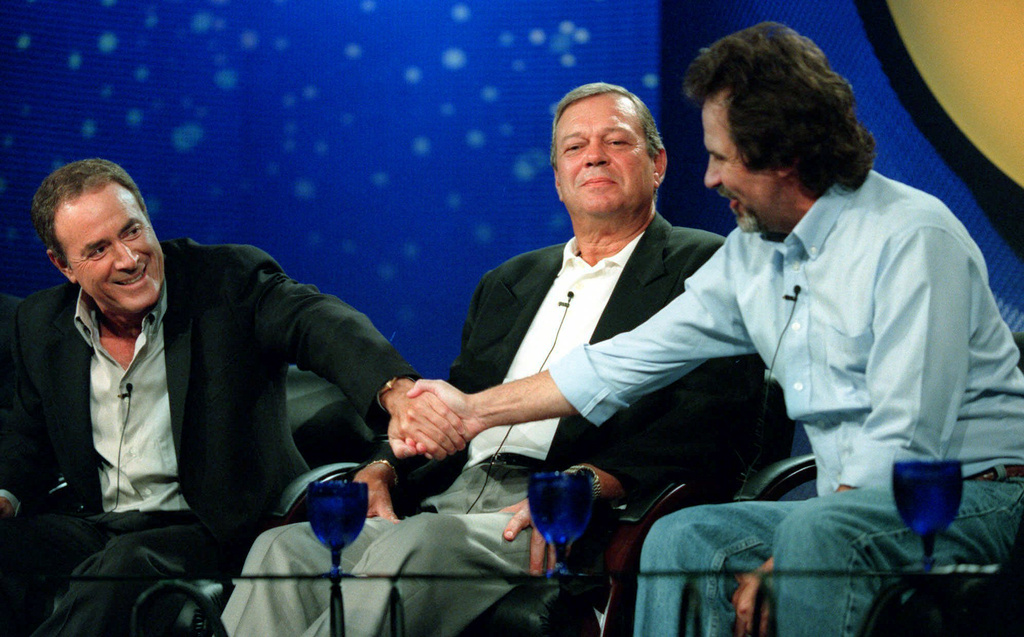 FILE - Al Michaels, a "Monday Night Football" play-by-play announcer, left, shakes hands with one of his new colleagues, comedian Dennis Miller, right, as executive producer Don Ohlmeyer looks on during a news conference at the ABC 2000 Summer Press Tour, July 16, 2000, in Pasadena, Calif. (AP Photo/Chris Pizzello, File)