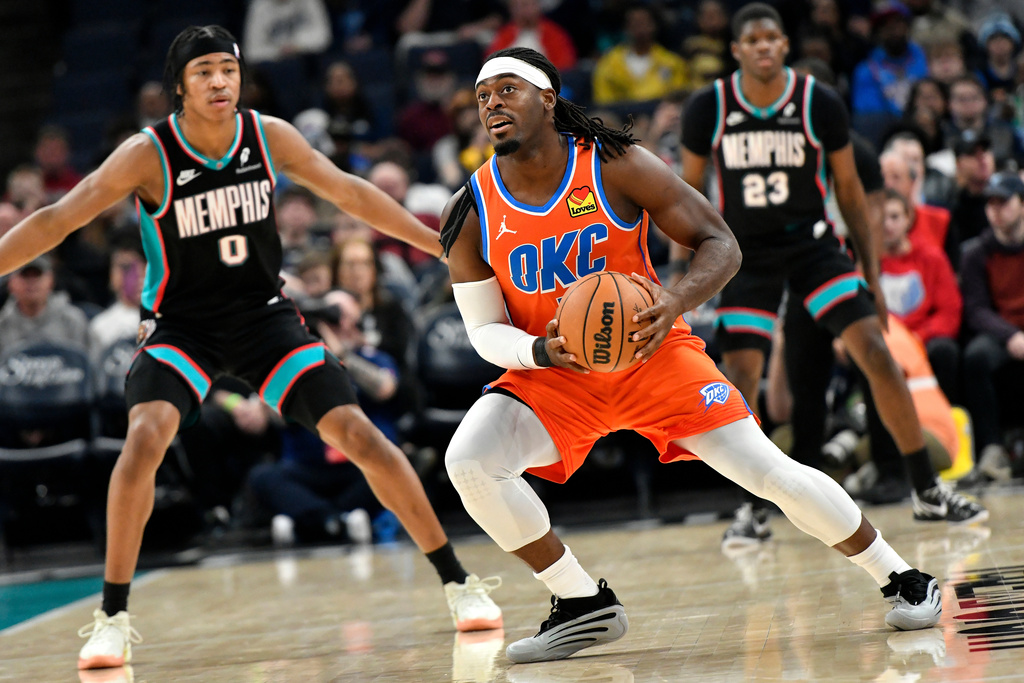 Oklahoma City Thunder guard Luguentz Dort handles the ball ahead of Memphis Grizzlies forward Jaylen Wells (0) and guard Cedric Coward (23) in the first half of an NBA basketball game Friday, Jan. 9, 2026, in Memphis, Tenn. (AP Photo/Brandon Dill)