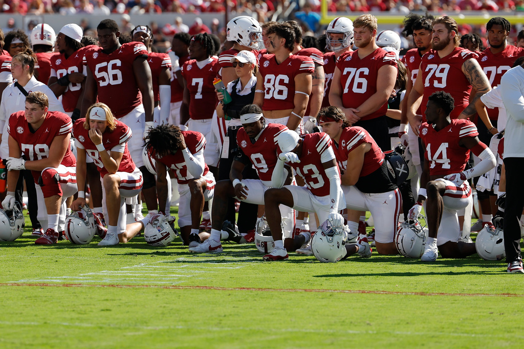 Oklahoma players take a knee as they wait to find out the status of teammate Keontez Lewis who collided with a wall on a catch-attempt during the first half of an NCAA college football game against Kent State, Saturday, Oct. 4, 2025, in Norman, Okla. (AP Photo/Alonzo Adams)