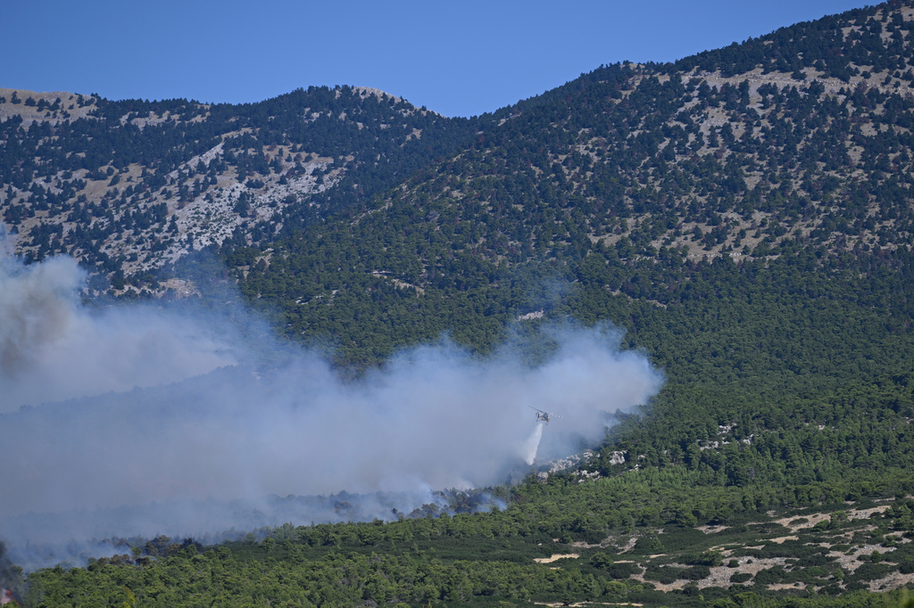 A firefighting helicopter drops water over a smoke-filled forest during a wildfire near Porto Germeno, northwest of Athens, Greece, Sunday, Aug. 2, 2026. (AP Photo/Michael Varaklas)