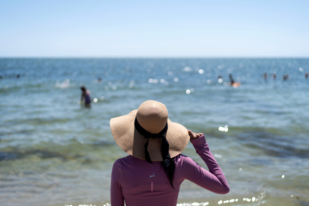 Ruth Wilson, who has lupus and is sensitive to the sun, stands at the water's edge while at the beach with family, Saturday, Aug. 16, 2025, in South Yarmouth, Mass. (AP Photo/David Goldman)
