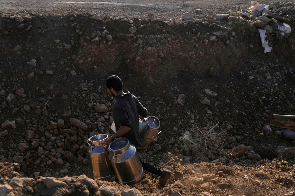 A Palestinian farmer carries containers of milk from their livestock across a trench dug by the Israeli army in a road leading to the West Bank hamlet of Khirbet Ras al-Ahmar, southeast of Tubas, on their way to sell it Saturday, Sept. 19, 2026. (AP Photo/Majdi Mohammed)
