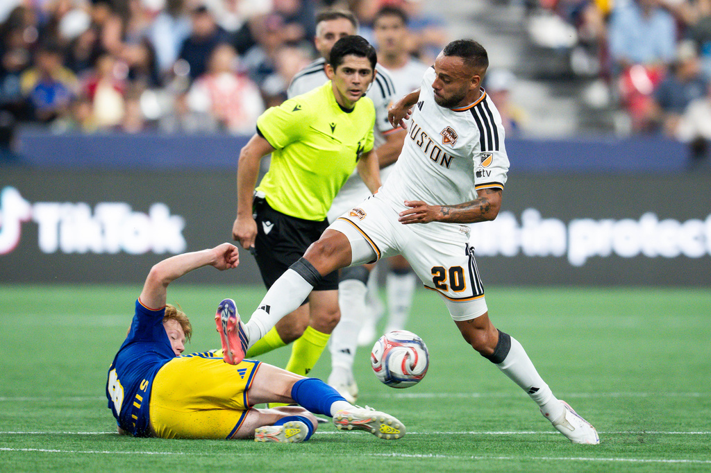 Vancouver Whitecaps' Oliver Larraz (bottom left) tackles Houston Dynamo FC's Guilherme Santos (20) during the first half of an MLS soccer match in Vancouver, B.C., on Wednesday, Aug. 19, 2026. (Ethan Cairns/The Canadian Press via AP)