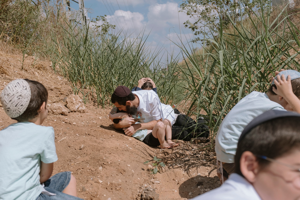 People take cover as a siren sounds a warning of incoming rockets fired from the Gaza Strip in Rehovot, Israel, Friday, Oct. 13, 2023. (AP Photo/Dor Kedmi)