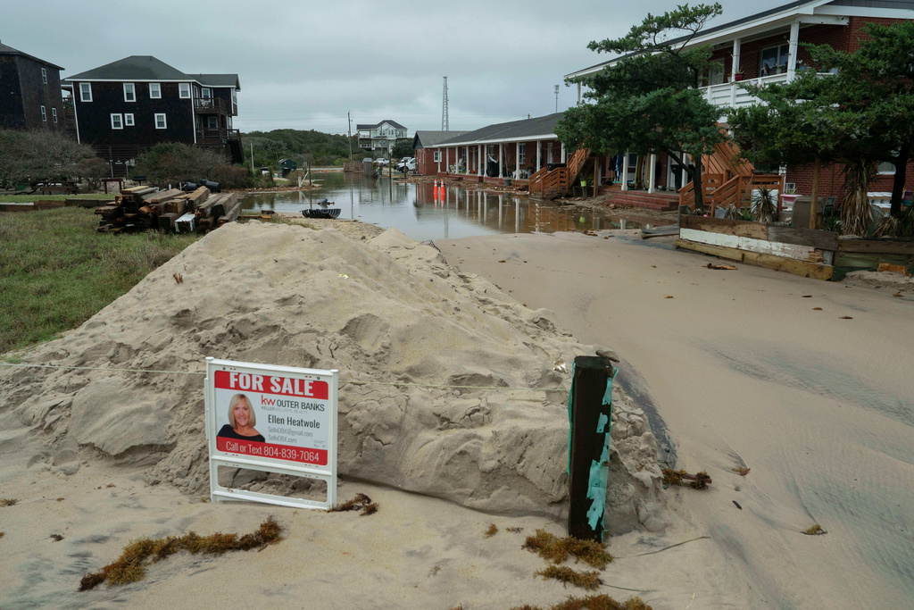 A "For Sale" sign its on a flooded road after a storm, Monday, Oct. 13, 2025, in Buxton, N.C. (AP Photo/Allison Joyce)