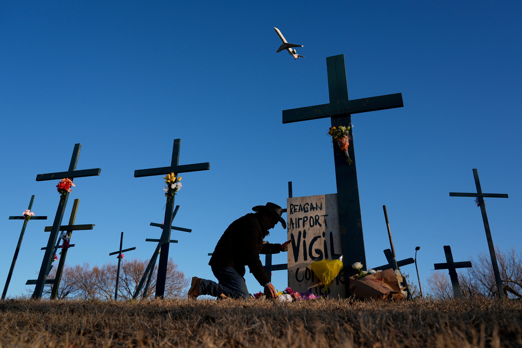 A plane takes off from Ronald Reagan Washington National Airport as Roberto Marquez of Dallas places flowers at a memorial of crosses he erected for the 67 victims of a midair collision between an Army helicopter and an American Airlines jet, Feb. 1, 2025, in Arlington, Va. (AP Photo/Carolyn Kaster, File)