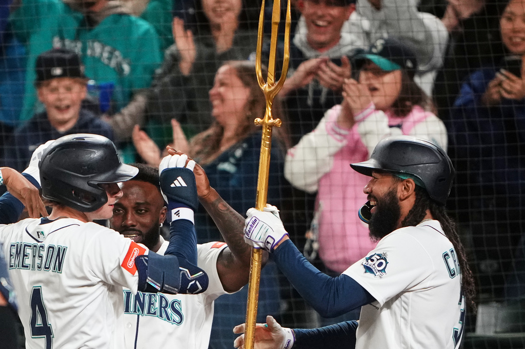 Seattle Mariners' J.P. Crawford, right, hands the trident to Colt Emerson (4) after Emerson hit a three-run home run against the Chicago White Sox, his first major league hit, during the eighth inning of a baseball game, Monday, May 18, 2026, in Seattle. (AP Photo/Lindsey Wasson)
