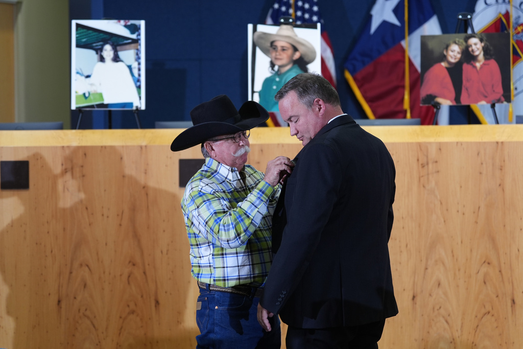 Austin Police Cold Case Detective Daniel Jackson, right, is given a pin that says "We Will Not Forget" by Bob Ayers, father of victim Amy Ayers, during a news conference regarding a breakthrough in the 1991 I Can't Believe It's Yogurt murder case, Monday, Sept. 29, 2025, in Austin, Texas. (AP Photo/Eric Gay)